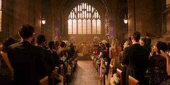 Movie still from “Secret Society of Second Born Royals” (2020), directed by Anna Mastro – A group of people sitting in a church with flowers; Extreme Wide shot, High angle