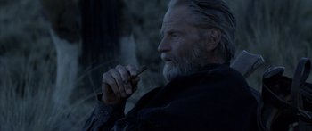 Movie still from “Blackthorn” (2011), directed by Mateo Gil – An older man smoking a cigarette while holding a cigar in his hand; Close Up shot, Over the shoulder angle