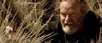Movie still from “Blackthorn” (2011), directed by Mateo Gil – An old man with a beard and a mustache is laying in the grass; Close Up shot, Low angle