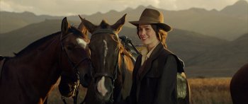 Movie still from “Blackthorn” (2011), directed by Mateo Gil – A woman standing next to two horses on a field; Medium shot, Over the shoulder angle