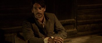 Movie still from “Blackthorn” (2011), directed by Mateo Gil – A man sitting at a table holding a glass of wine; Medium shot, Over the shoulder angle
