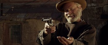 Movie still from “Blackthorn” (2011), directed by Mateo Gil – An older man holding a gun and smiling; Close Up shot, Over the shoulder angle