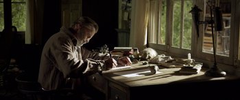 Movie still from “Blackthorn” (2011), directed by Mateo Gil – A man sitting at a desk writing on a piece of paper; Medium shot, Low angle