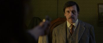Movie still from “Blackthorn” (2011), directed by Mateo Gil – A man sitting in a chair holding a gun; Close Up shot, Over the shoulder angle