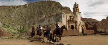 Movie still from “Blackthorn” (2011), directed by Mateo Gil – A group of men riding horses in front of an old building; Extreme Wide shot, Low angle