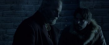 Movie still from “Blackthorn” (2011), directed by Mateo Gil – An old man with a long white beard standing next to a brick wall; Close Up shot, Over the shoulder angle