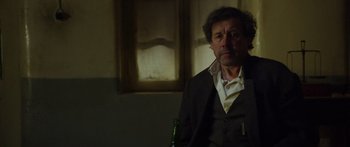 Movie still from “Blackthorn” (2011), directed by Mateo Gil – A man sitting in a chair with a bottle in his hand; Medium shot, Over the shoulder angle