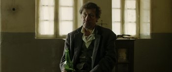 Movie still from “Blackthorn” (2011), directed by Mateo Gil – A man sitting in a chair holding a bottle of beer; Medium shot, Over the shoulder angle