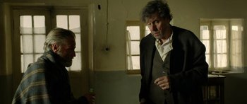 Movie still from “Blackthorn” (2011), directed by Mateo Gil – A man in a suit is talking to another man in front of a window; Medium shot, Over the shoulder angle