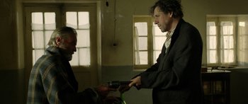 Movie still from “Blackthorn” (2011), directed by Mateo Gil – Two men in a room exchanging a gun; Medium shot, Low angle