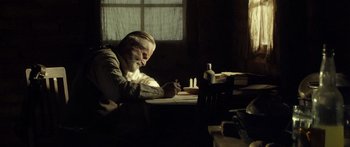 Movie still from “Blackthorn” (2011), directed by Mateo Gil – An old man sitting at a table writing on a piece of paper; Medium shot, Over the shoulder angle