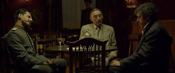 Movie still from “Blackthorn” (2011), directed by Mateo Gil – An older man sitting at a table with a glass of wine; Medium shot, Over the shoulder angle