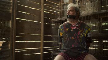 Movie still from “Sentinelle” (2023), directed by David Caviglioli – An older man sitting in a chair with his mouth taped shut; Medium shot, High angle