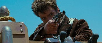 Movie still from “Serenity” (2005), directed by Joss Whedon – A man holding a gun while standing in front of a camera; Close Up shot, Low angle