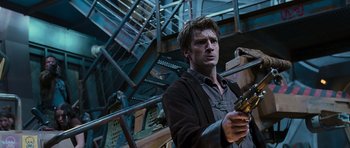 Movie still from “Serenity” (2005), directed by Joss Whedon – A man standing in front of stairs holding a cell phone; Medium shot, Low angle