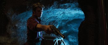 Movie still from “Serenity” (2005), directed by Joss Whedon – A man holding a gun in front of a cave; Medium shot, Low angle