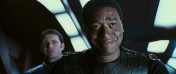 Movie still from “Serenity” (2005), directed by Joss Whedon – A man in a black shirt is smiling for the camera; Close Up shot, Over the shoulder angle