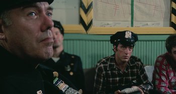 Movie still from “Serpico” (1973), directed by Sidney Lumet – A group of men sitting next to each other in a room; Close Up shot, Over the shoulder angle