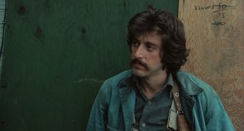 Movie still from “Serpico” (1973), directed by Sidney Lumet – A man with long hair and a beard is sitting in front of a green wall; Close Up shot, Over the shoulder angle
