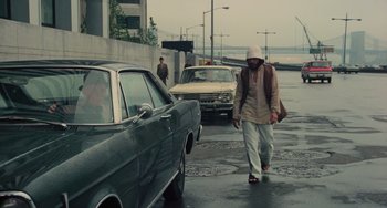 Movie still from “Serpico” (1973), directed by Sidney Lumet – A man walking down a street next to parked cars; Wide shot, Low angle