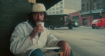 Movie still from “Serpico” (1973), directed by Sidney Lumet – A man sitting on the side of the road eating a sandwich; Medium shot, Low angle