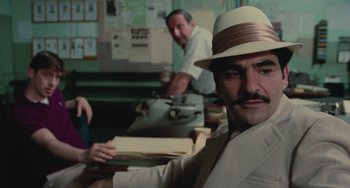 Movie still from “Serpico” (1973), directed by Sidney Lumet – A man in a hat and a suit sitting in front of a desk; Close Up shot, Over the shoulder angle