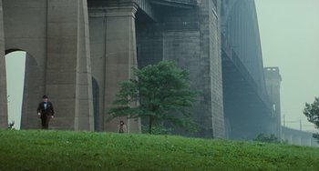 Movie still from “Serpico” (1973), directed by Sidney Lumet – A person standing next to a tree in front of a bridge; Extreme Wide shot, High angle