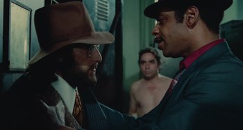 Movie still from “Serpico” (1973), directed by Sidney Lumet – A man in a hat and a tie is talking to another man in a suit and tie; Medium shot, Over the shoulder angle