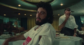 Movie still from “Serpico” (1973), directed by Sidney Lumet – A man sitting at a table in front of other people; Medium shot, Low angle