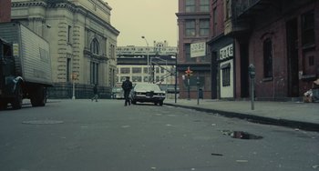 Movie still from “Serpico” (1973), directed by Sidney Lumet – A man standing on the side of the road next to an old car; Extreme Wide shot, High angle