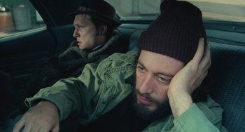 Movie still from “Serpico” (1973), directed by Sidney Lumet – A man with a beard sitting next to another man in the back of a car; Close Up shot, High angle