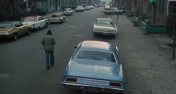 Movie still from “Serpico” (1973), directed by Sidney Lumet – A woman walking down a street past parked cars; Extreme Wide shot, High angle