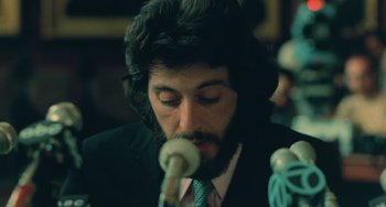 Movie still from “Serpico” (1973), directed by Sidney Lumet – A man in a suit and tie is playing a microphone; Close Up shot, Low angle