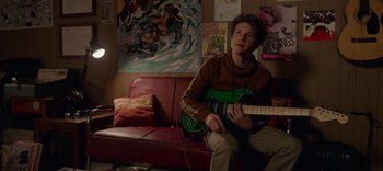 A man sitting on a red couch holding a green guitar