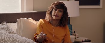 Movie still from “Blockers” (2018), directed by Kay Cannon – A woman sitting on a couch holding a cell phone; Medium shot, Over the shoulder angle