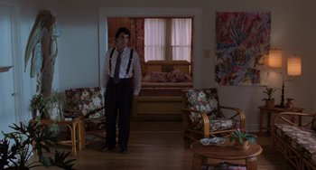 Movie still from “Sex, Lies, and Videotape” (1989), directed by Steven Soderbergh – A man standing in a living room wearing suspenders; Wide shot, High angle