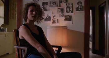 Movie still from “Sex, Lies, and Videotape” (1989), directed by Steven Soderbergh – A woman sitting in a chair in front of a wall of pictures; Medium shot, Low angle