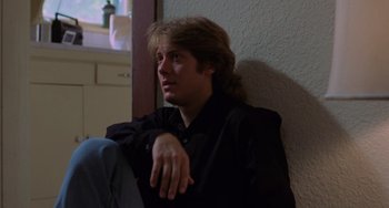 Movie still from “Sex, Lies, and Videotape” (1989), directed by Steven Soderbergh – A man sitting on the ground in front of a wall; Medium shot, Low angle