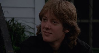 Movie still from “Sex, Lies, and Videotape” (1989), directed by Steven Soderbergh – A man with long brown hair sitting in front of a building; Close Up shot, Low angle