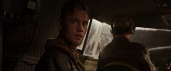 Movie still from “Shadow in the Cloud” (2020), directed by Roseanne Liang – A young man is sitting on a bus looking at the camera; Close Up shot, Low angle