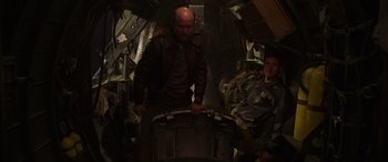 Movie still from “Shadow in the Cloud” (2020), directed by Roseanne Liang – A bald man with a bald head is standing in a room with other men; Medium shot, High angle