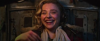 Movie still from “Shadow in the Cloud” (2020), directed by Roseanne Liang – A young woman with headphones is smiling for the camera; Close Up shot, Low angle