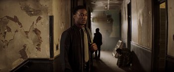Movie still from “Shaft” (2019), directed by Tim Story – A man standing in a hallway with a woman standing behind him; Medium shot, Over the shoulder angle