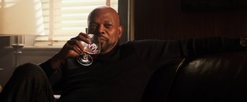 Movie still from “Shaft” (2019), directed by Tim Story – A man sitting in a chair holding a glass of wine; Medium shot, Low angle