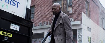 Movie still from “Shaft” (2019), directed by Tim Story – A man in a trench coat holding an umbrella in front of a brick building; Medium shot, Low angle