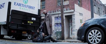 Movie still from “Shaft” (2019), directed by Tim Story – A man in a trench coat is on the ground next to another man in a trench coat; Wide shot, Low angle