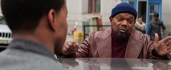 Movie still from “Shaft” (2019), directed by Tim Story – A man sitting at a table with another man holding a cigarette; Medium shot, Over the shoulder angle