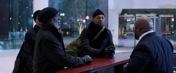 Movie still from “Shaft” (2019), directed by Tim Story – Two men are sitting at a table in front of a building; Medium shot, Over the shoulder angle