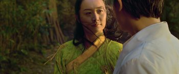 Movie still from “Shang-Chi and the Legend of the Ten Rings” (2021), directed by Destin Daniel Cretton – A woman in a green and yellow dress looking into the camera; Close Up shot, Over the shoulder angle
