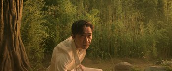 Movie still from “Shang-Chi and the Legend of the Ten Rings” (2021), directed by Destin Daniel Cretton – A man sitting in front of some trees; Medium shot, Low angle